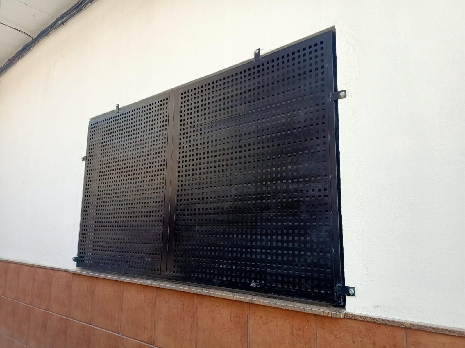 cierre de chapa perforada negra instalado en una ventana, vista en escorzo