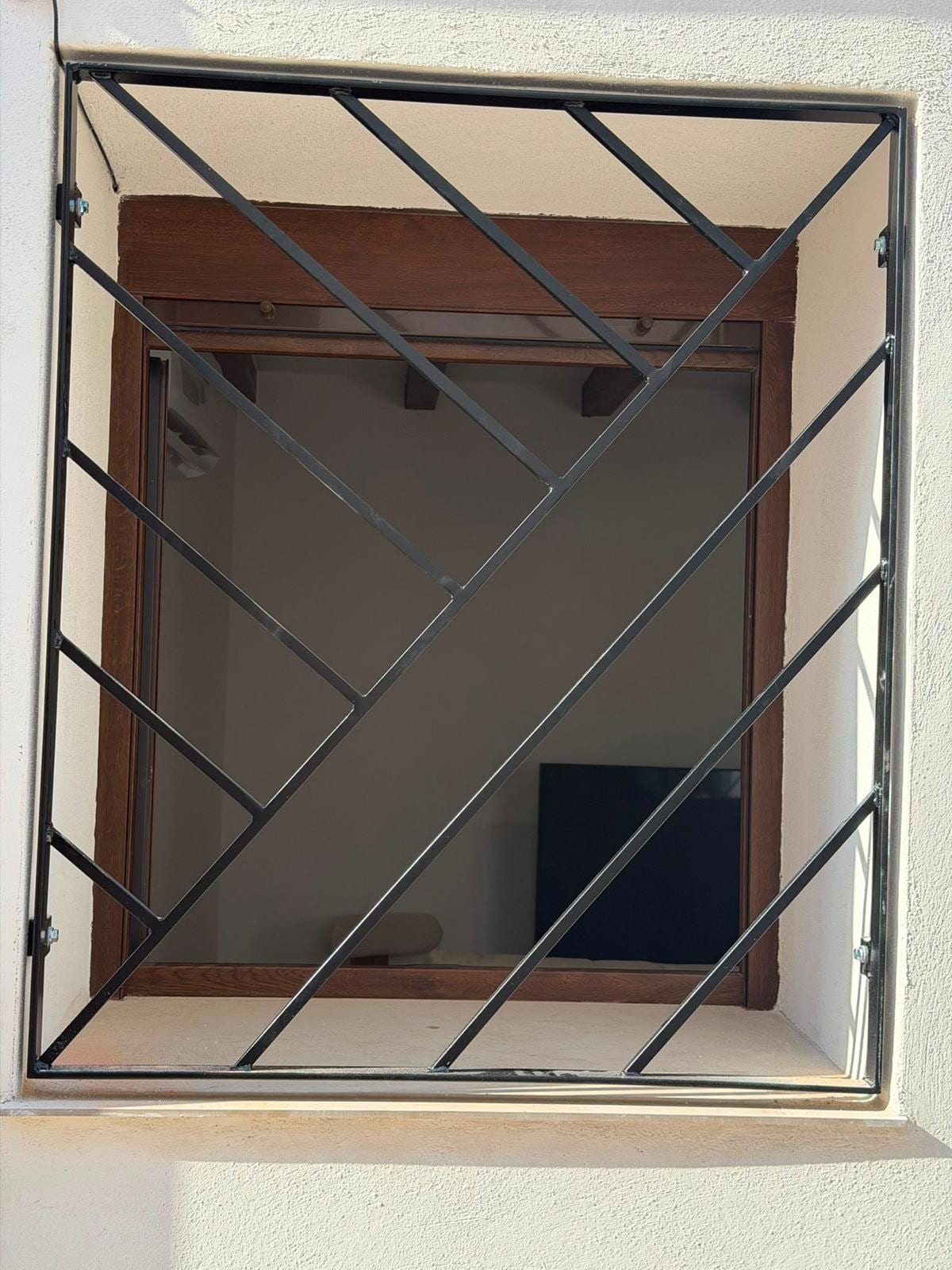 La misma reja negra instalada vista con la persiana subida, dejando ver el marco de madera de la ventana.
